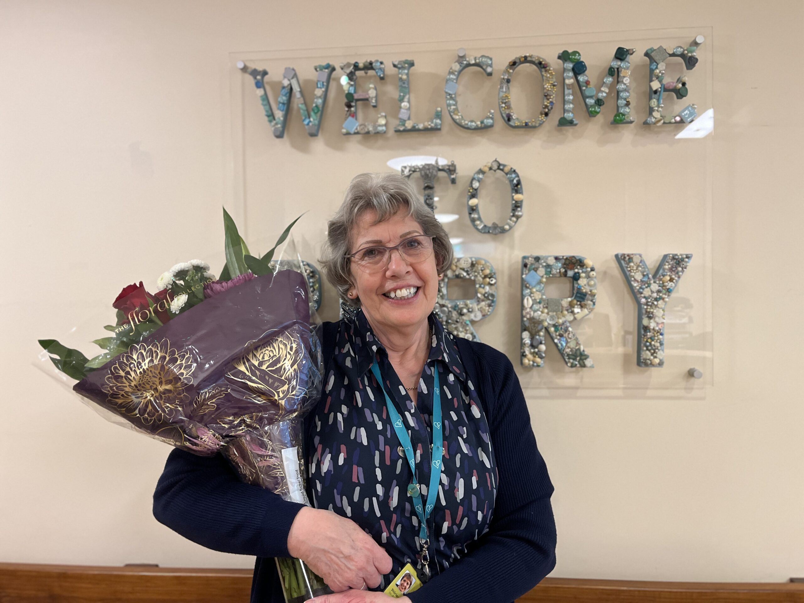 Shirley standing in front of Perry Ward sign holding bouquet of flowers