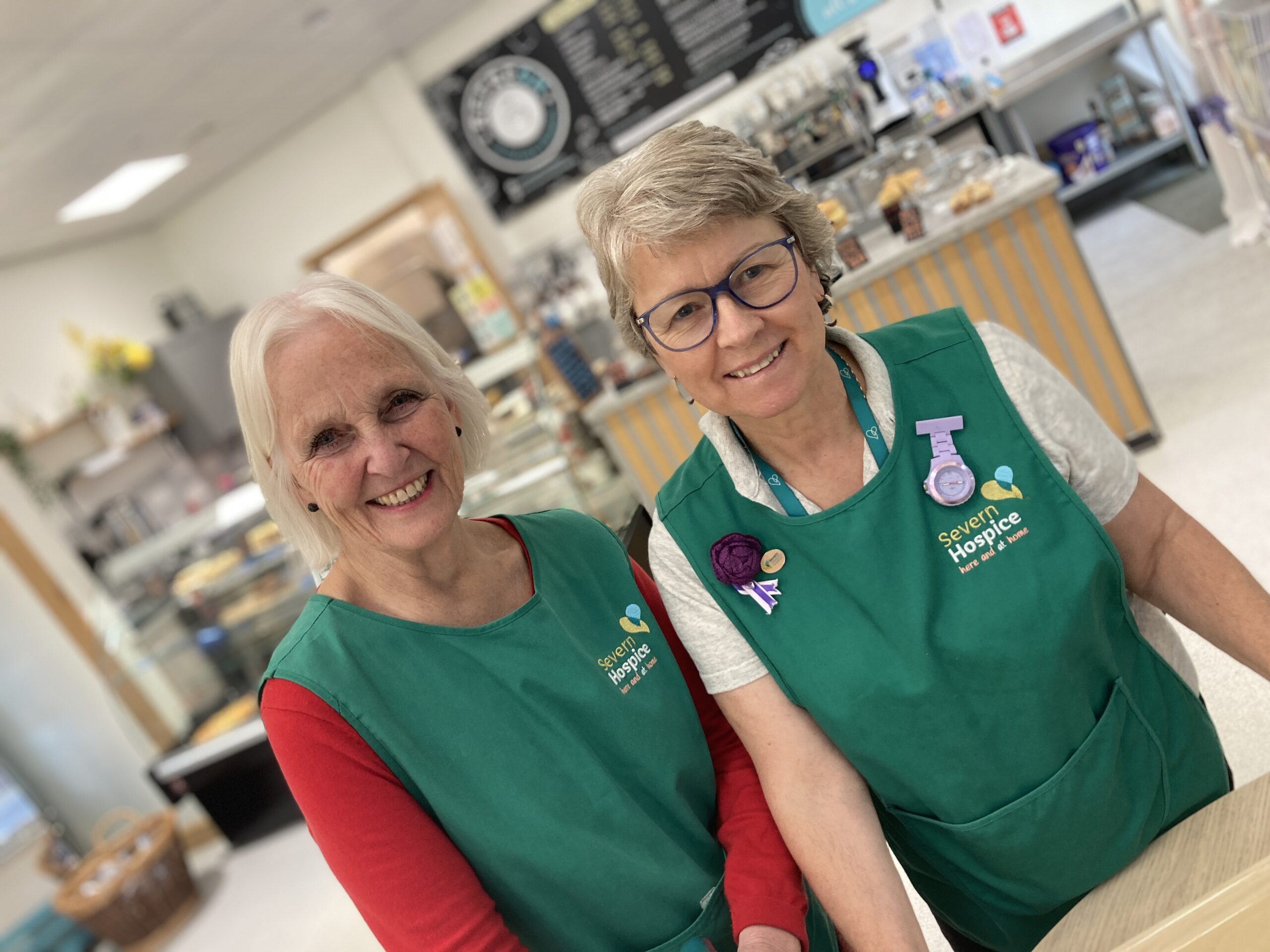 Two people in green tabards serving in a cafe
