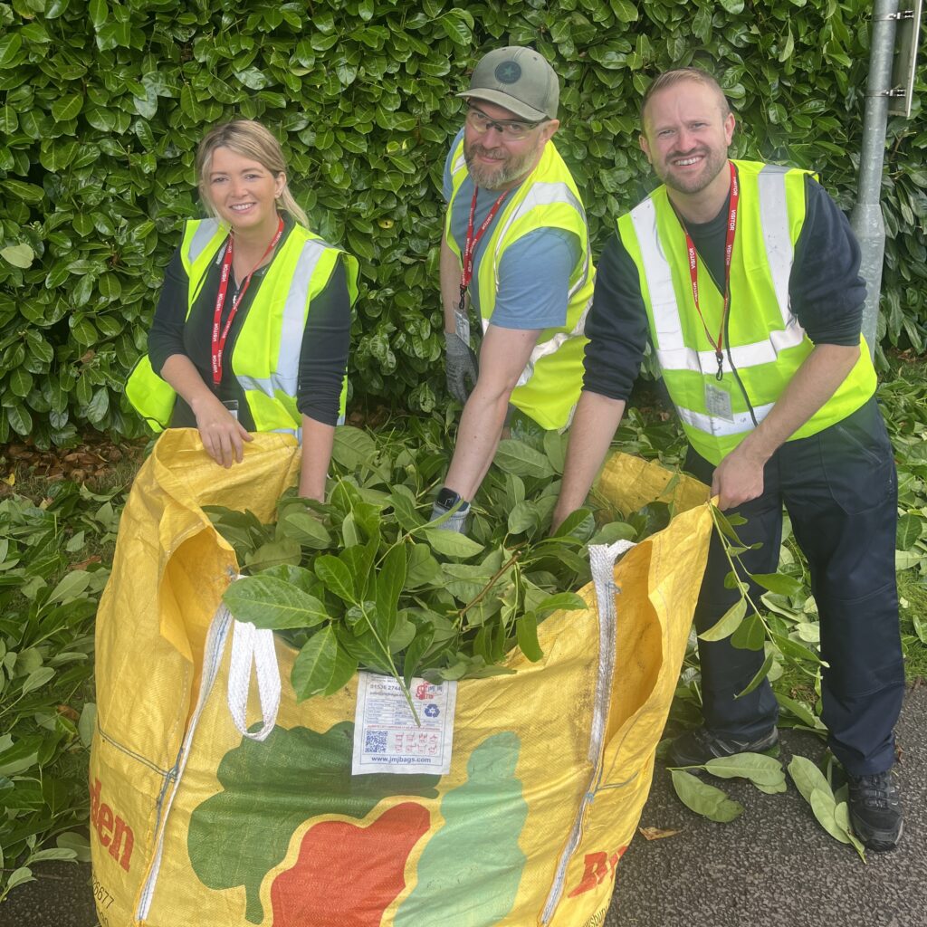 Three people in high-viz waistcoats putting in hedge trimmings into a large sack