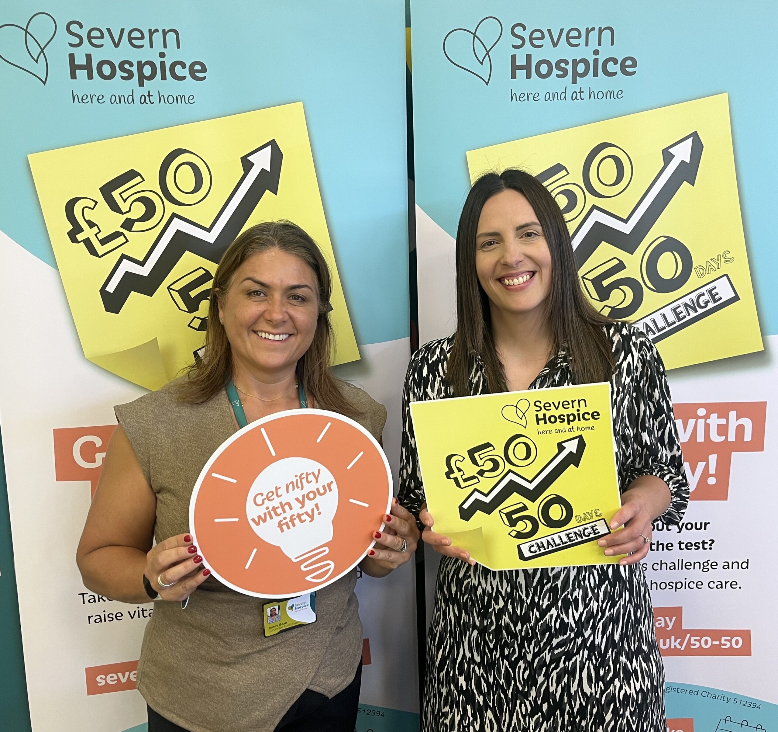 Two people standing together holding photo props - one is a yellow post-it note and the other is in the shape of a light bulb