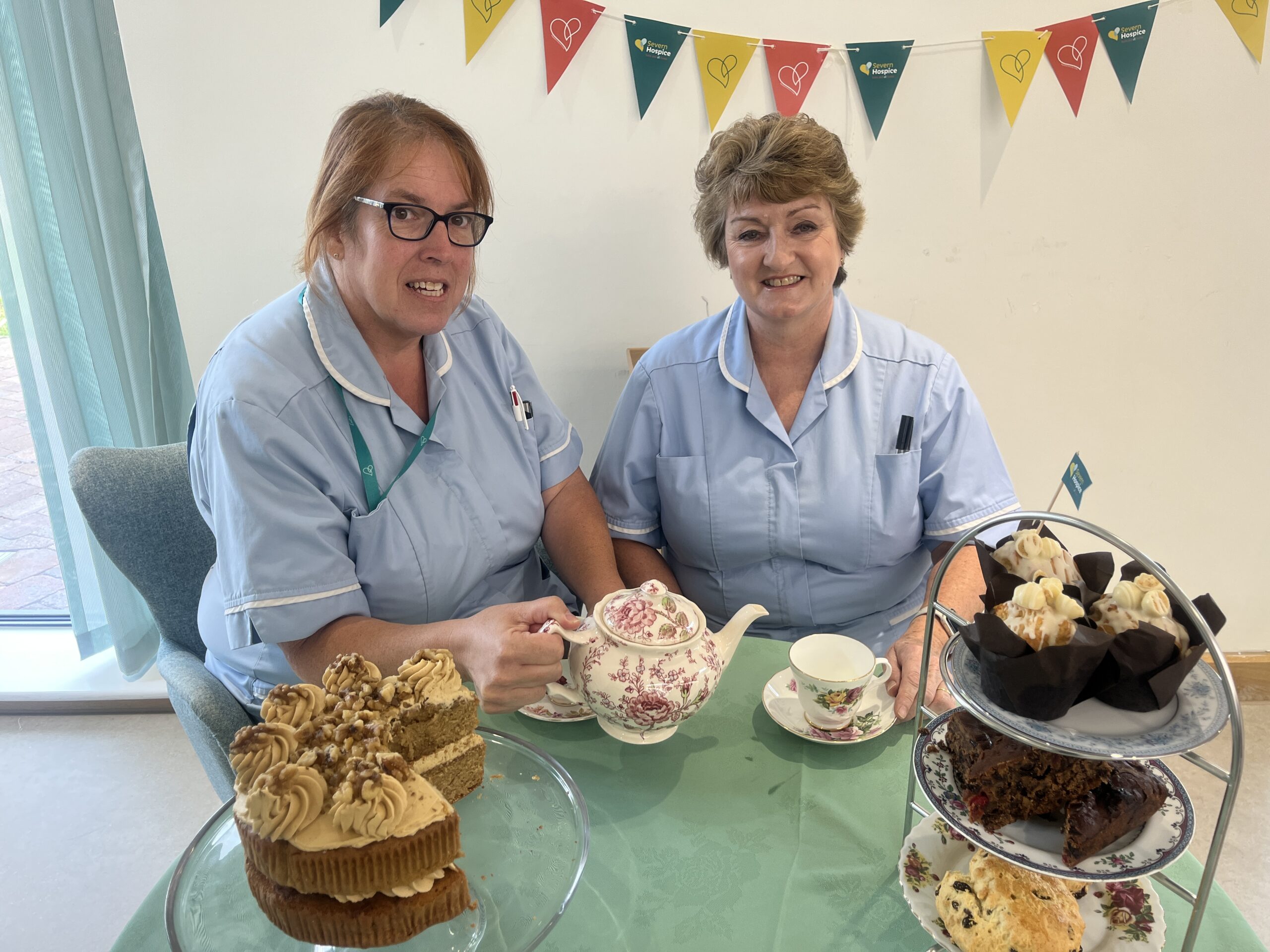 Two health care assistants sitting at a table with teapot, china cups and cakes