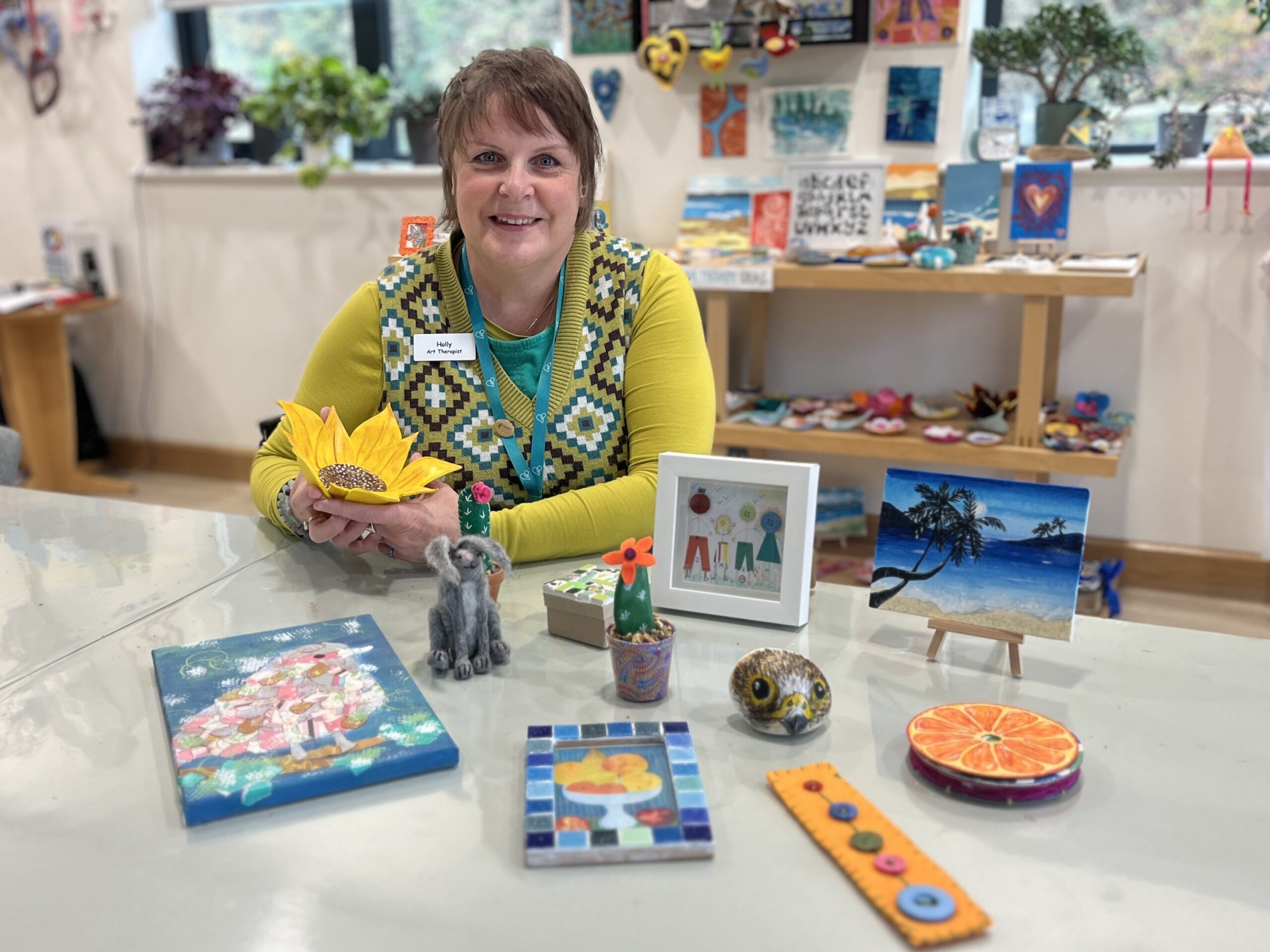 Person in yellow cardigan sitting at a table with a range of pieces of art.