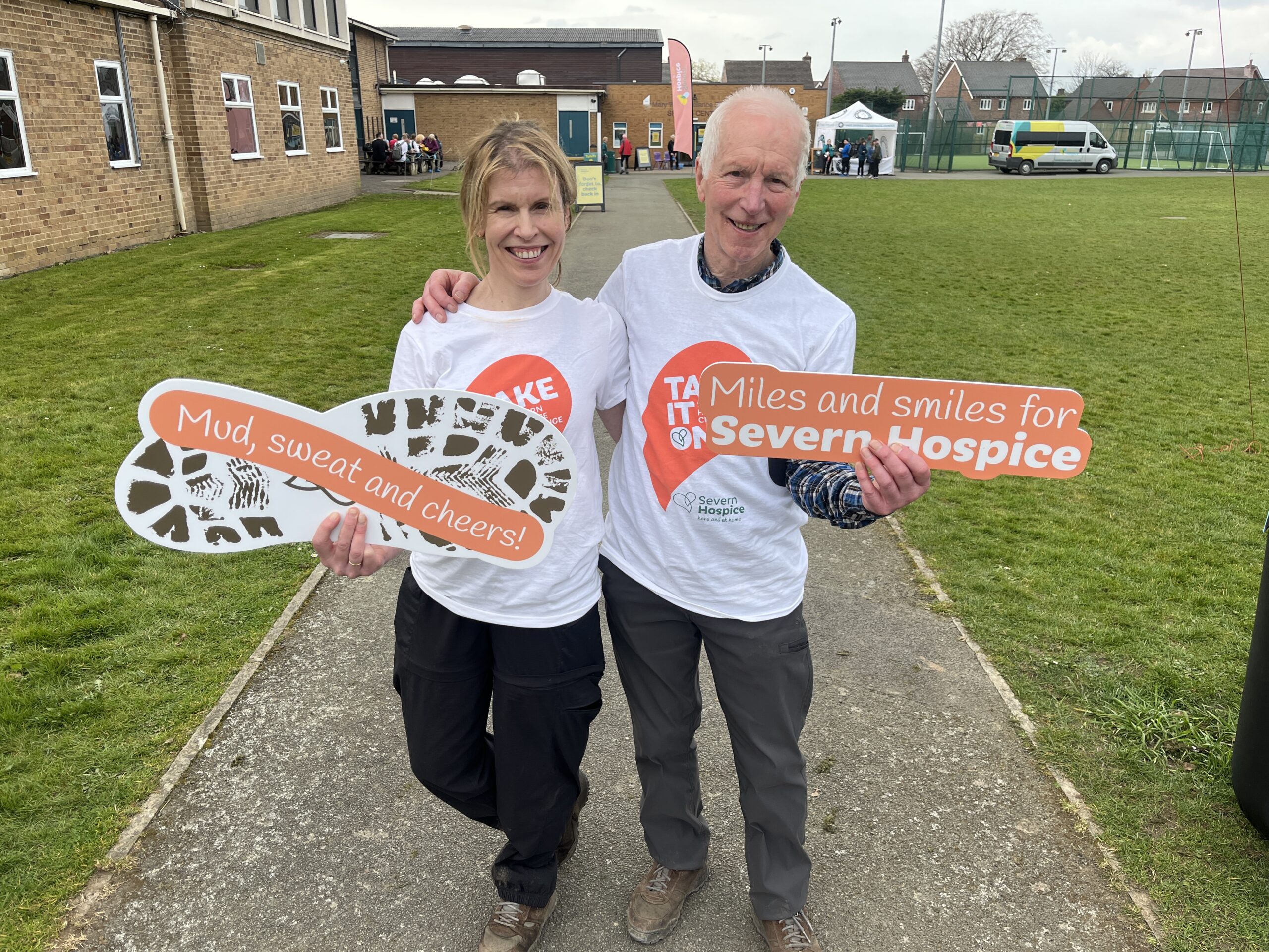 Two walkers holding photo props that say 'mud, sweat and cheers' and 'Miles and smiles for Severn Hospice'.