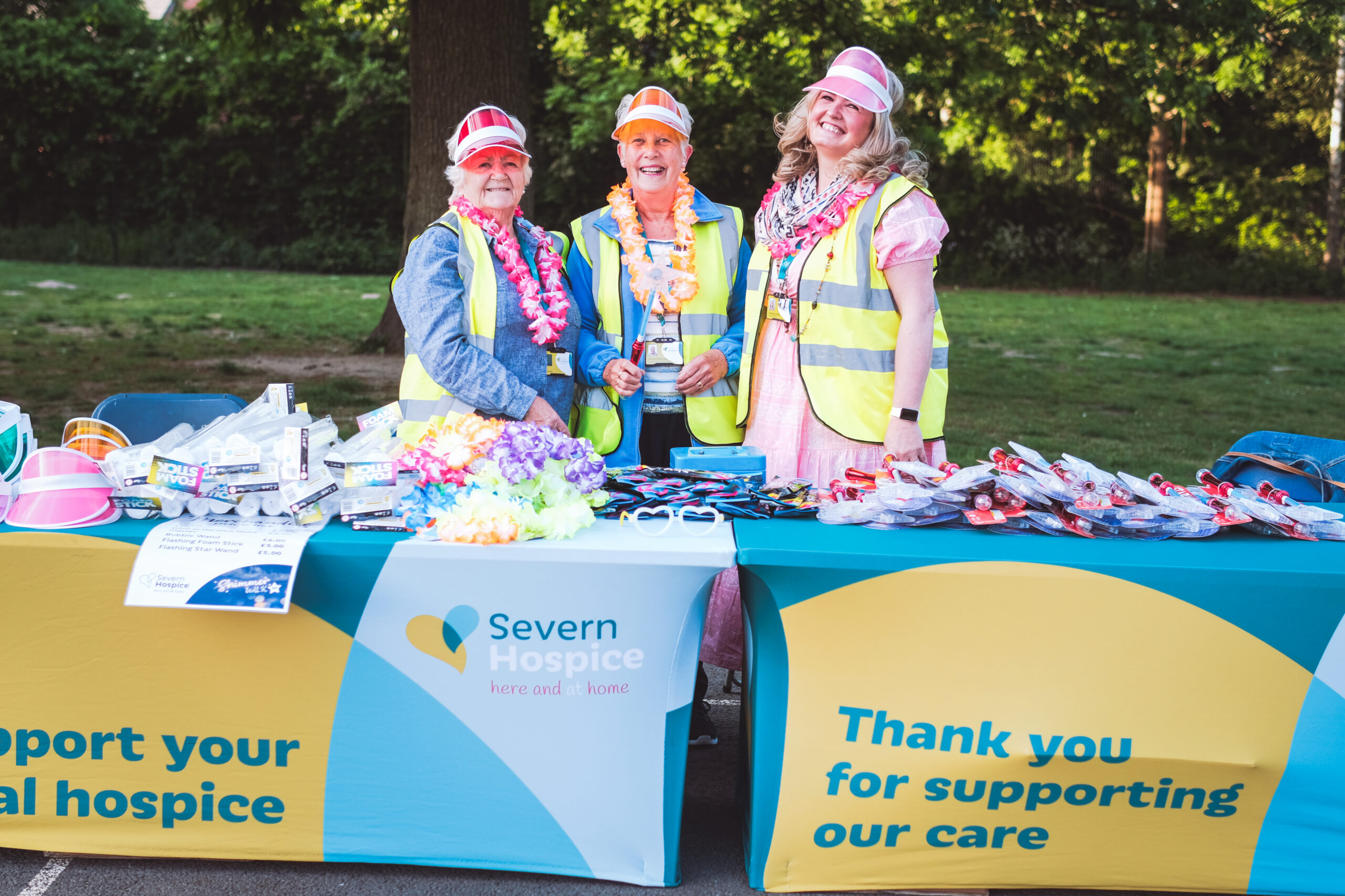Three people in high-viz vests at a table full of brightly coloured merchandise